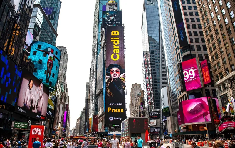A busy pedestrian square lined with digital billboards of many sizes, each running a different advertiser