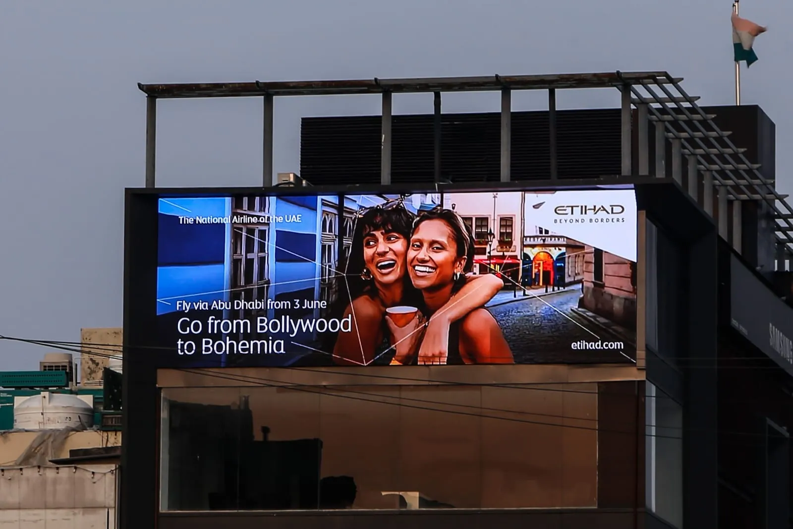 Outdoor LED screen running an advertisement on the top floor of a commercial building under a grey evening sky